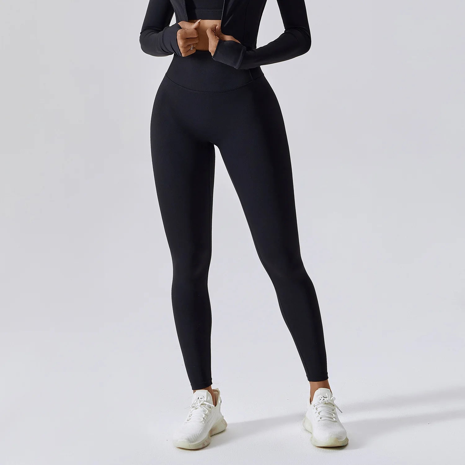 Person wearing black leggings and a black long-sleeve top on a light gray background